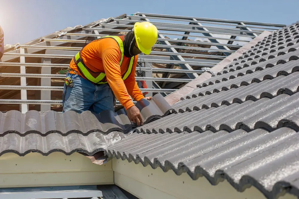 Roof repair, worker with white gloves replacing gray tiles or shingles on house with blue sky