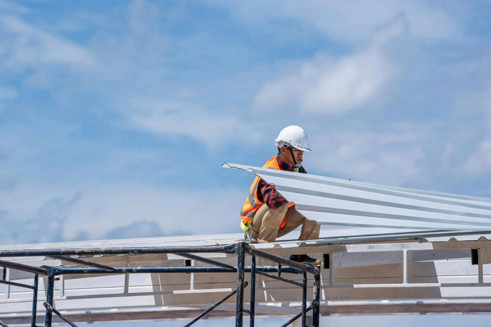 Worker with roofer tools wearing protective gear installing new roof on top roof at construction site